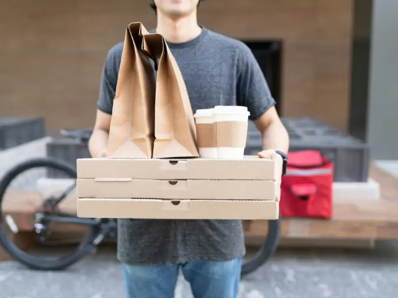 The image is a medium close-up of a food delivery person holding a substantial order.