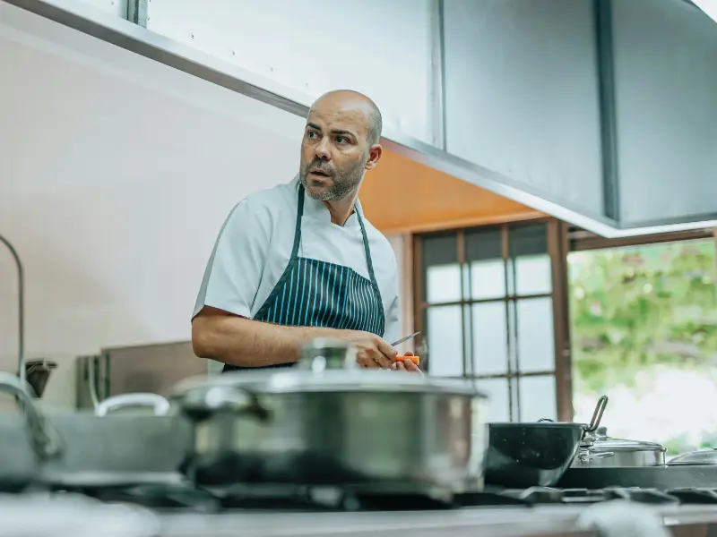 This image is a portrait of a chef in a professional kitchen. He is a man
