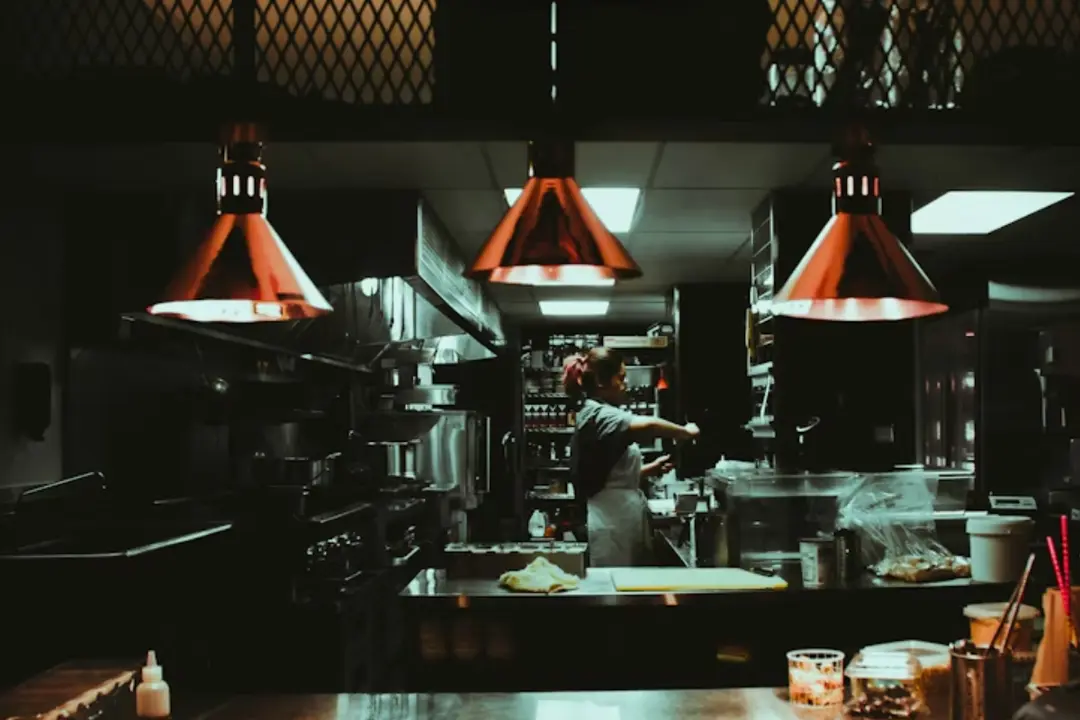 The image shows a professional kitchen, resembling a dark kitchen or a dedicated food-production space for delivery.