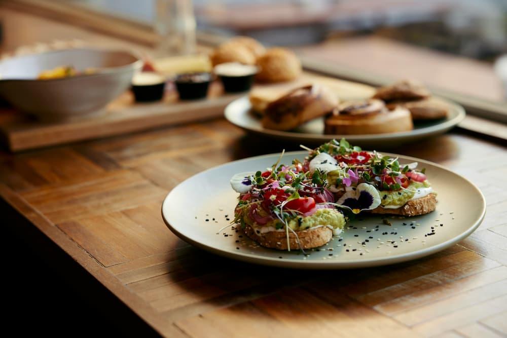 A colorful dish with toasts topped with avocado, tomato, fresh herbs, and edible flowers