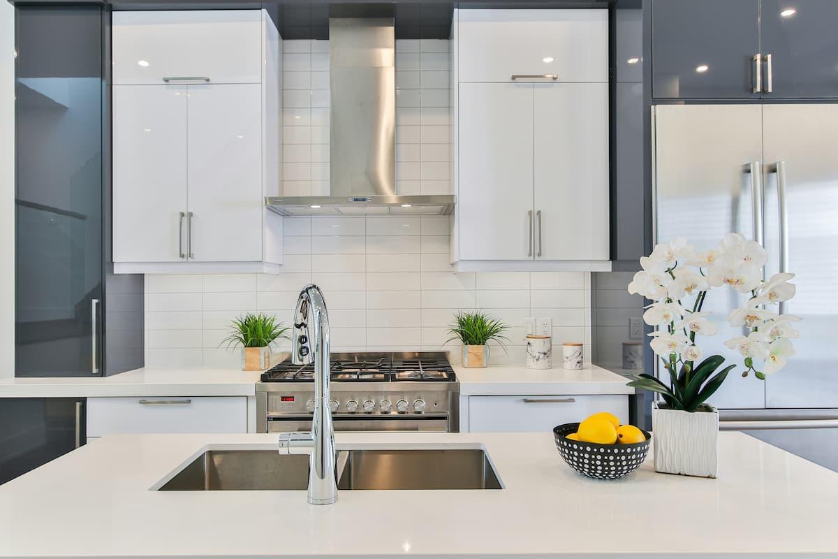 Modern kitchen with sleek white and gray cabinets, stainless steel appliances, and a center island with a sink, decorated with potted plants and fresh lemons.