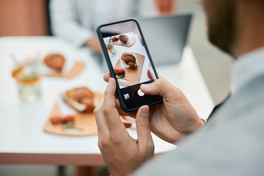 Restaurant manager taking a photo of plates with croissants and fruits on a table, highlighting the gastronomic experience