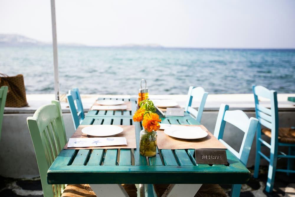 A table decorated by the sea, with colorful chairs, white plates, and a reserved sign ready for lunch at a restaurant