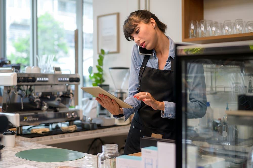Manager managing reservations at a café using a tablet while talking on the phone.