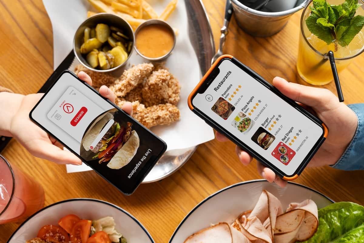 Two people browsing food apps on phones at a restaurant, showing how a restaurant chatbot​​​​ can enhance the ordering experience.