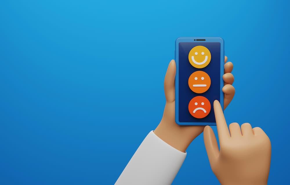 Hand holding a phone with three facial expression icons on a blue screen