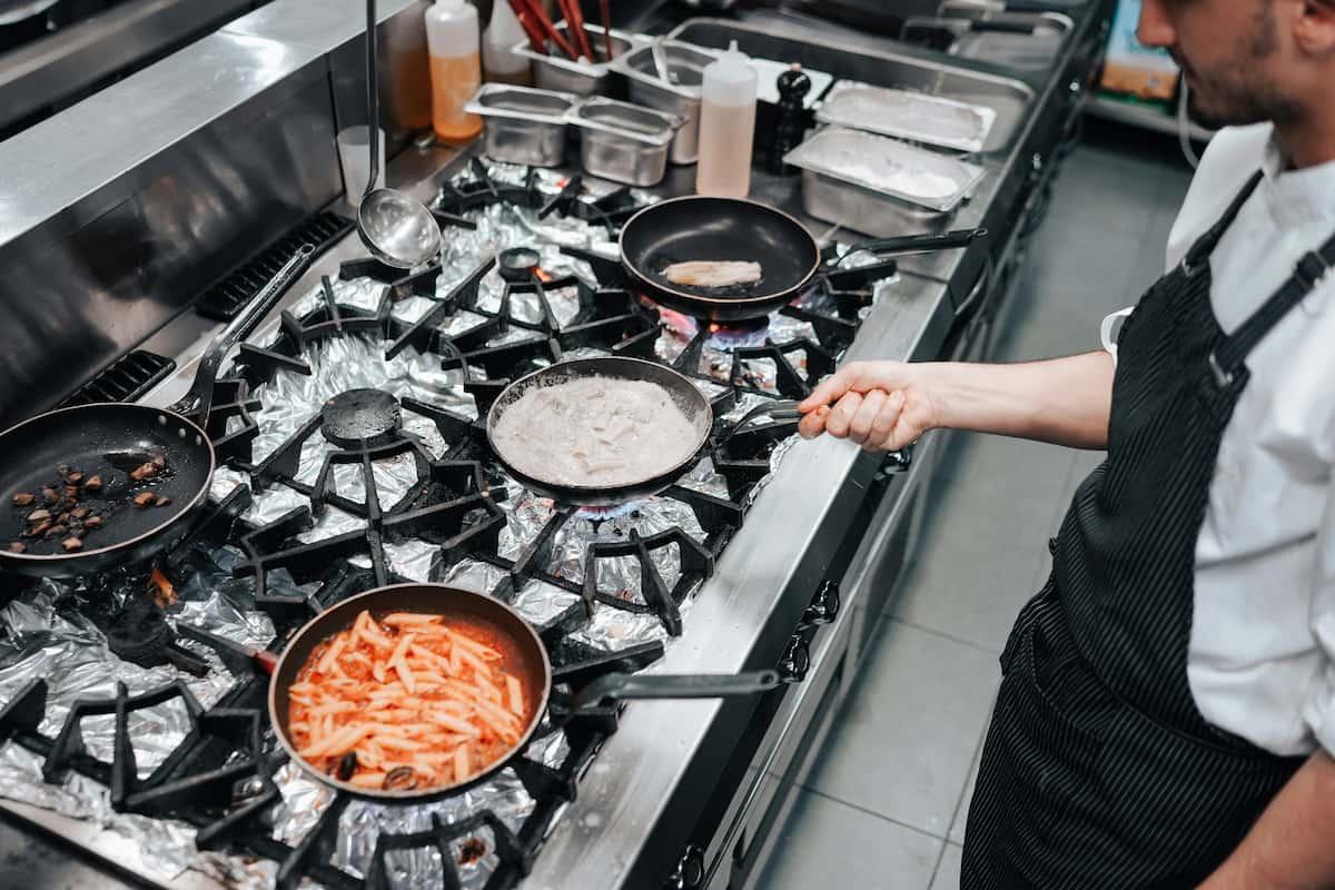 Chef cooking multiple dishes at once on a large stove, perfect example of scaling up food production​​​​ in a kitchen.
