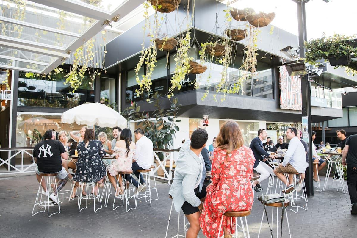 A bustling restaurant scene showcasing spring restaurant promotions, featuring guests enjoying meals in an outdoor seating area adorned with lush greenery and hanging plants.