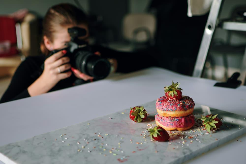 A photographer capturing the image of colorful donuts decorated with strawberries and sprinkles on a marble table