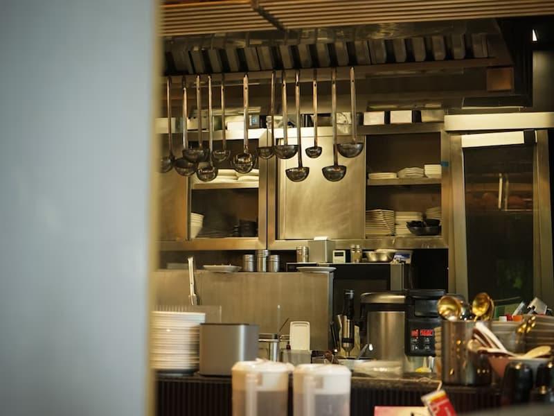 Industrial kitchen neatly arranged with hanging utensils, shelves holding plates, and stainless steel preparation equipment.