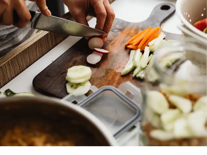 Person slicing vegetables on a clean cutting board during a food hygiene inspection to ensure proper kitchen safety standards.