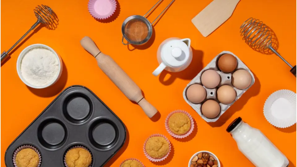 This image shows a vibrant, top-down view of baking ingredients and tools arranged on a bright orange background.
