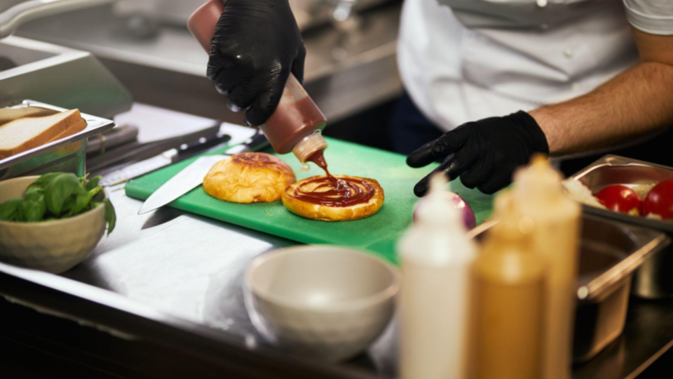 This image captures a professional chef at work in a commercial kitchen, focusing on the assembly of a gourmet burger.