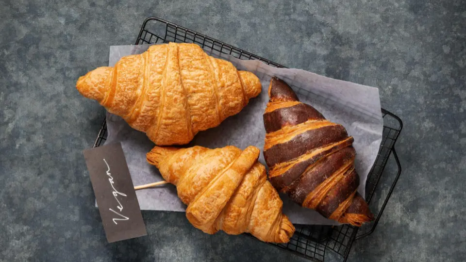 This is a flat lay (top-down) shot of three croissants resting on parchment paper inside a black wire cooling rack.
