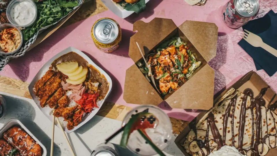 This is a dynamic photograph that shows various street food dishes, including a hearty portion of breaded chicken with white rice, a box of poke, and another dessert with a chocolate sauce.