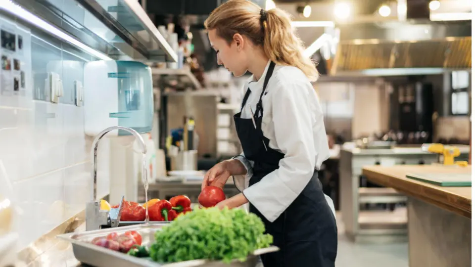 The image shows a young woman working in a professional commercial kitchen.