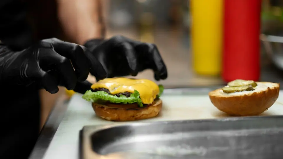 This image provides a close-up, action-oriented look at the assembly of a classic cheeseburger in a professional kitchen.