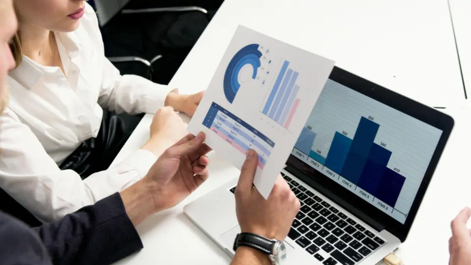 Several professionals are gathered around a white desk, focusing on performance metrics.