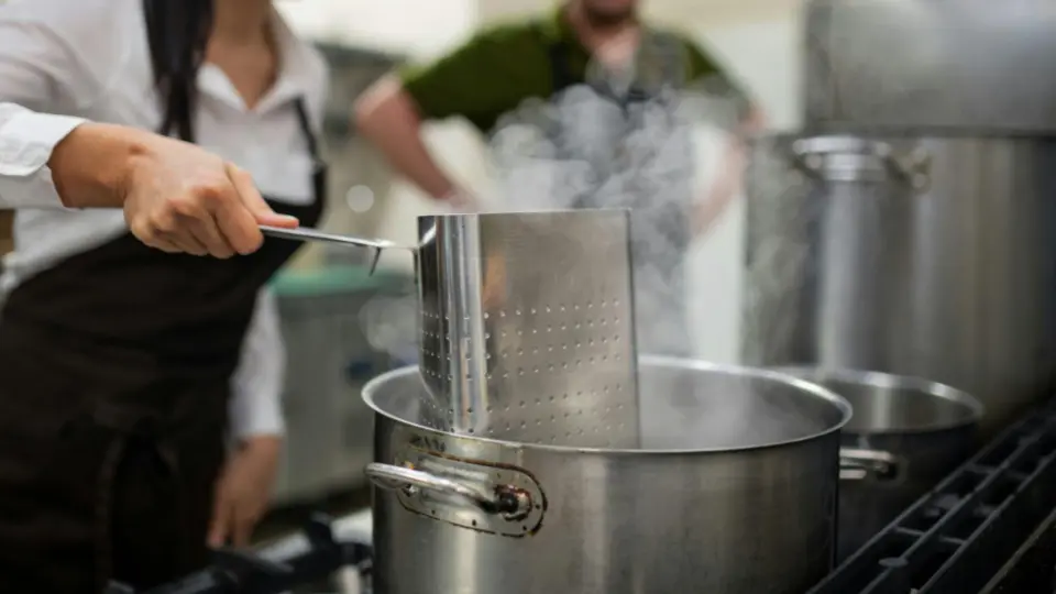 This image captures an action shot of a chef working at a boiling station in a professional kitchen.