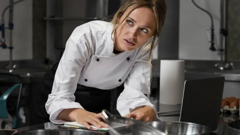 This image captures the intense and fast-paced nature of managing a modern commercial kitchen, focusing on a female chef in a moment of high concentration.