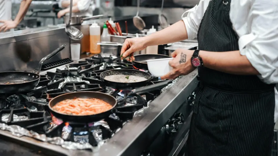 This action-oriented shot captures a chef adding the final touches to multiple dishes during a busy service.