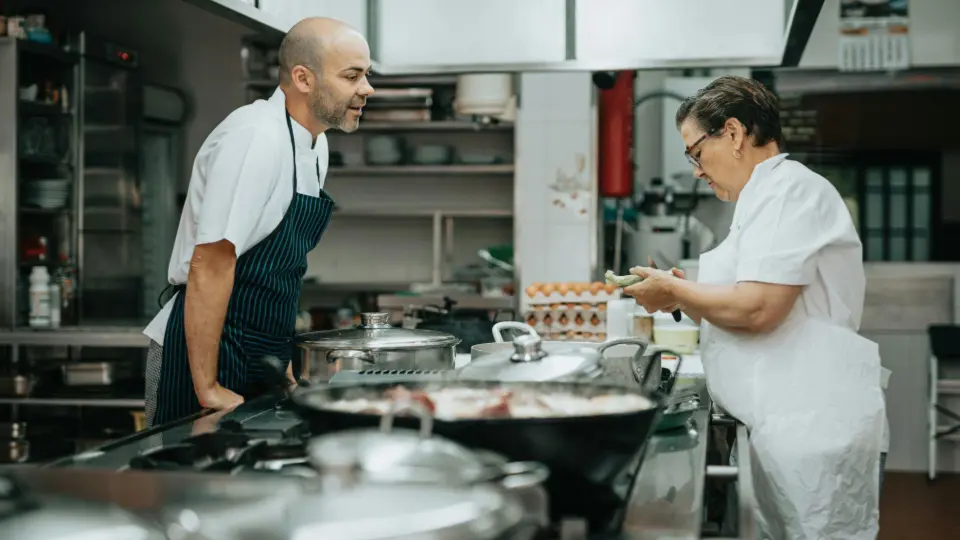 This image captures a heartfelt, candid moment between two kitchen professionals in a traditional commercial kitchen.