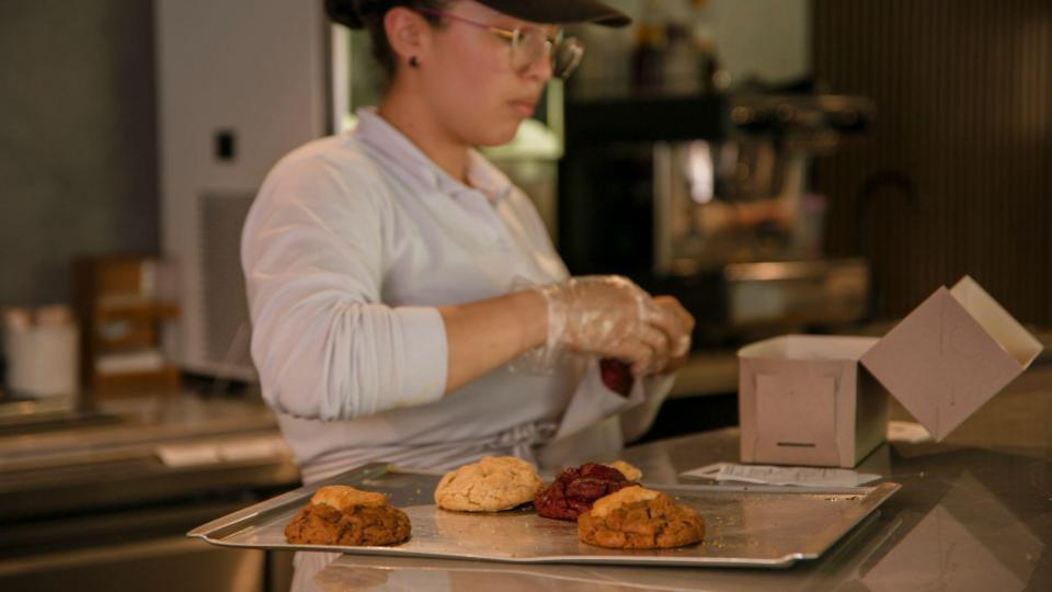 A young woman working in a bakery or cafe, focused on packaging products.