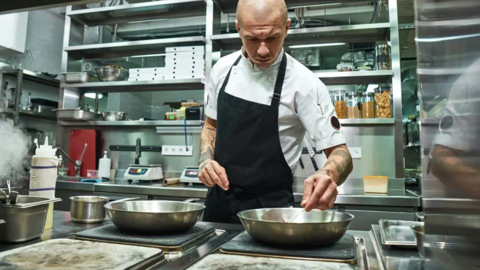This image captures a chef focusing on the final flavor profile of a dish in a modern commercial kitchen.