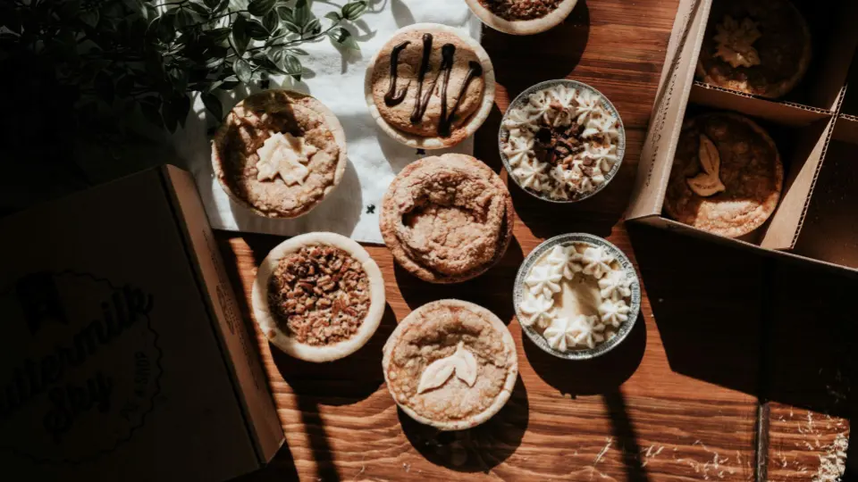 This is a flat lay photograph with dramatic high-contrast lighting (chiaroscuro), showing an assortment of artisanal mini pies.