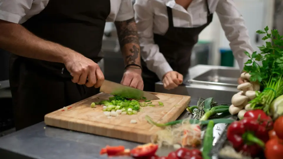 This image shows two culinary professionals working together at a stainless steel prep station.