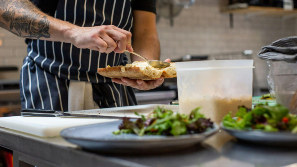 This image captures the meticulous final assembly of a sandwich in a professional kitchen.