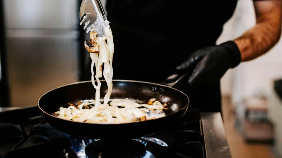 O Gemini disse
This image captures a professional chef performing a high-heat culinary technique in a commercial kitchen setting.