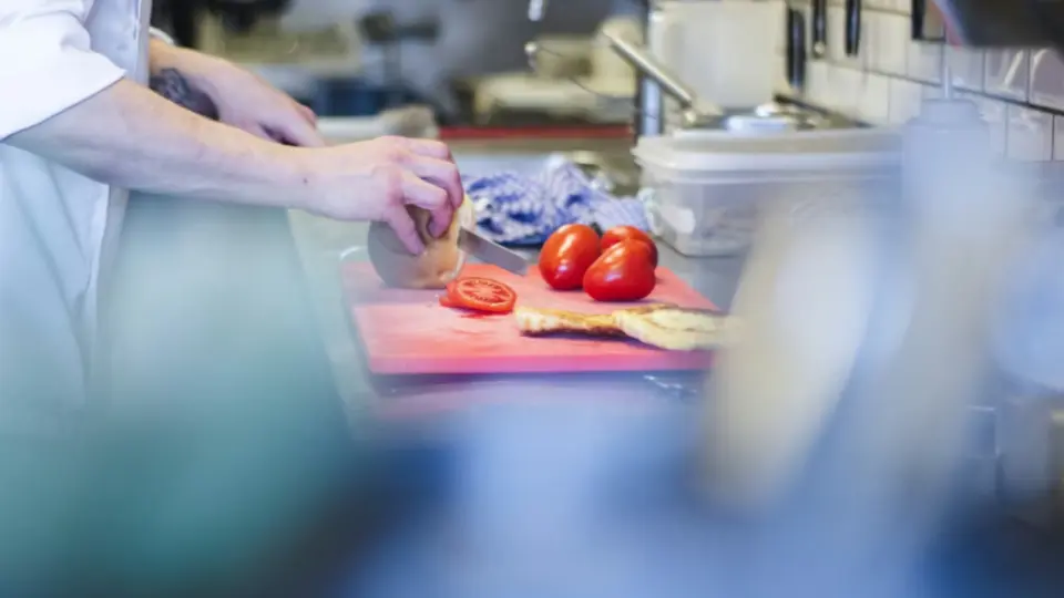 The image shows a chef working in a professional kitchen, preparing ingredients on a cutting board.