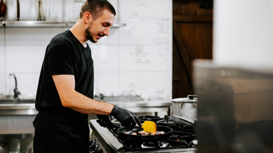 This shot focuses on a chef managing a single dish on a commercial range.