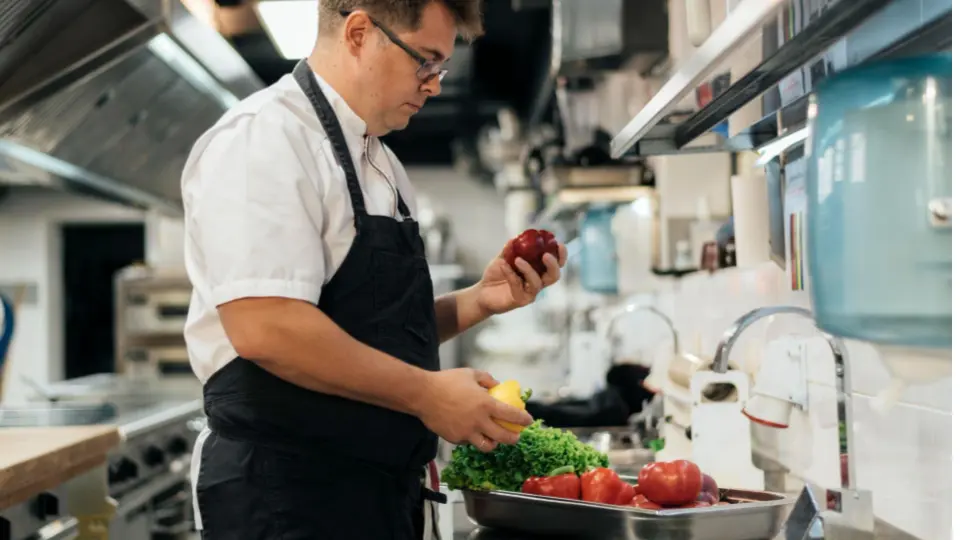 This image shows a professional chef carefully selecting fresh produce in a commercial kitchen environment.