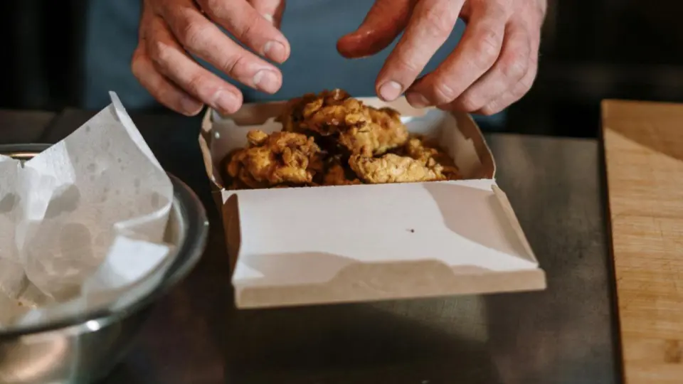 This image captures a close-up, action shot of a person preparing a takeaway meal.