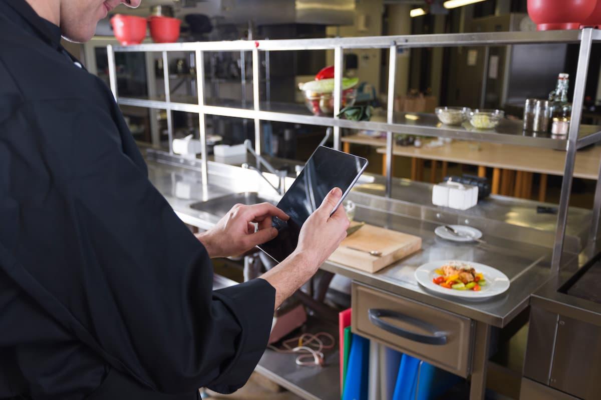 Chef using tablet in a commercial kitchen, showing the benefits of central production kitchens for efficiency and control.