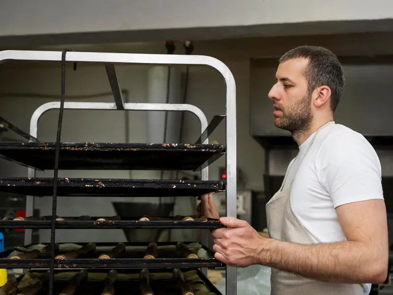 The image is a medium close-up of a baker or chef working in a commercial kitchen or bakery setting.