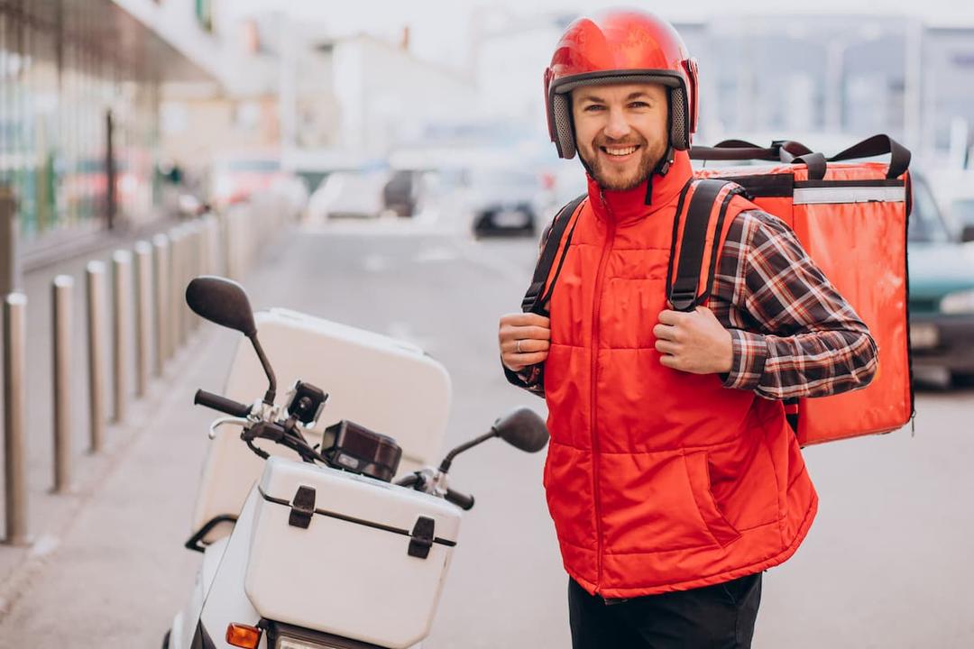 Smiling courier next to scooter ready for delivery, illustrating efficient food delivery route optimization in urban areas.