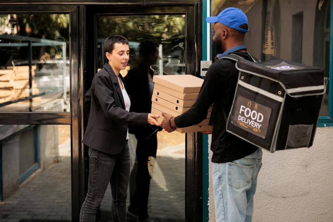 Food delivery with a courier handing pizza boxes to a customer at the entrance of a building. The scene highlights the convenience of food delivery services.