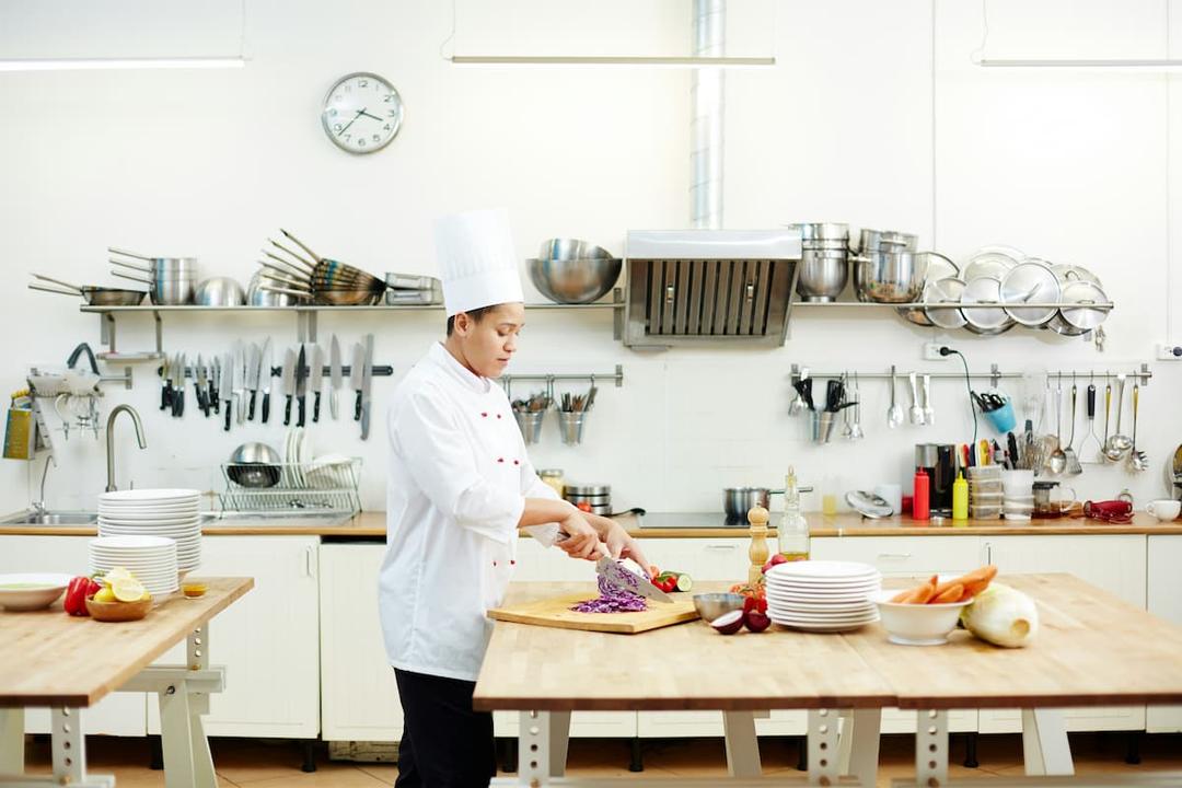 Professional chef preparing fresh vegetables at a dark kitchen setup, featuring industrial-grade equipment, organized utensils, and a clean workspace.