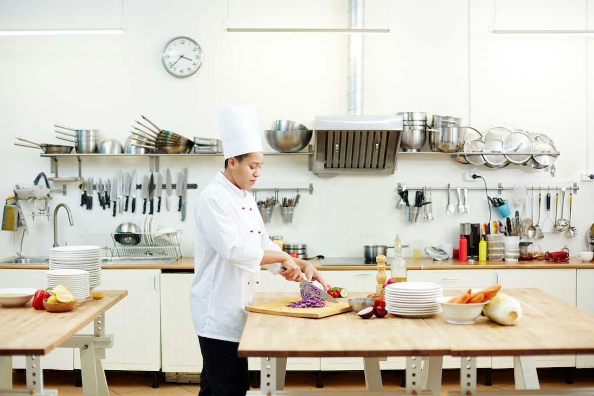 Professional chef preparing fresh vegetables at a dark kitchen setup, featuring industrial-grade equipment, organized utensils, and a clean workspace.