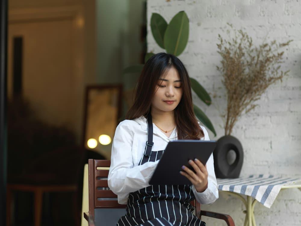 Restaurant manager with an apron working on a tablet in a cozy and modern setting.