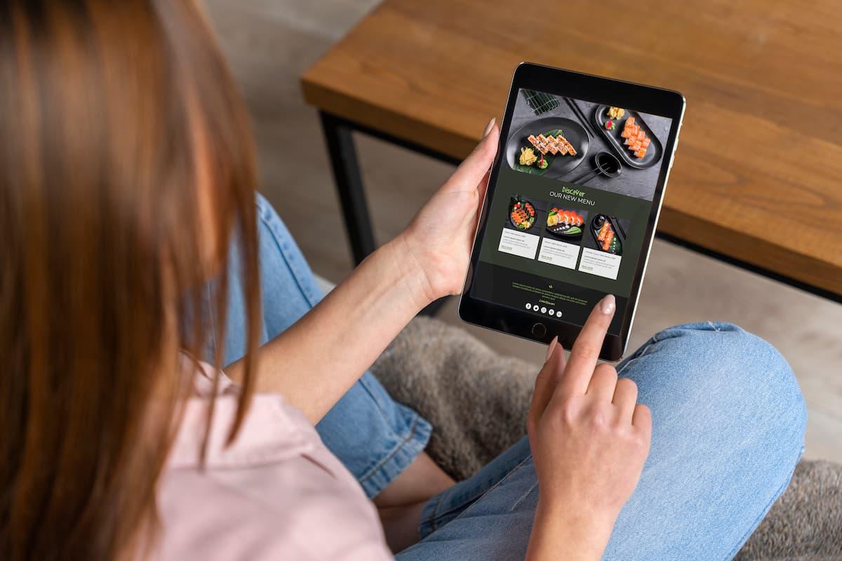 Woman browsing a sushi menu on a tablet, illustrating how to create a digital menu board for modern restaurant use.