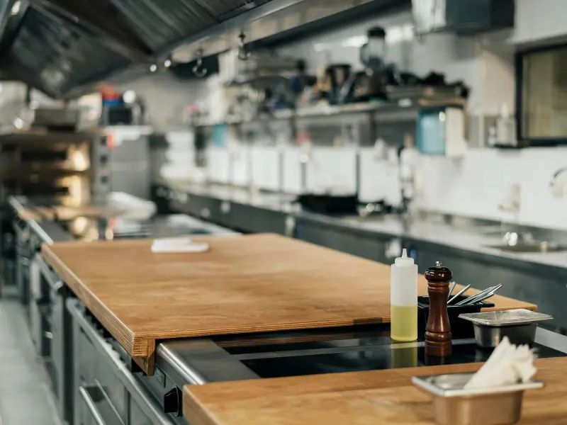 This image provides a view of a professional, commercial kitchen, focusing on a central wooden work surface in the foreground.