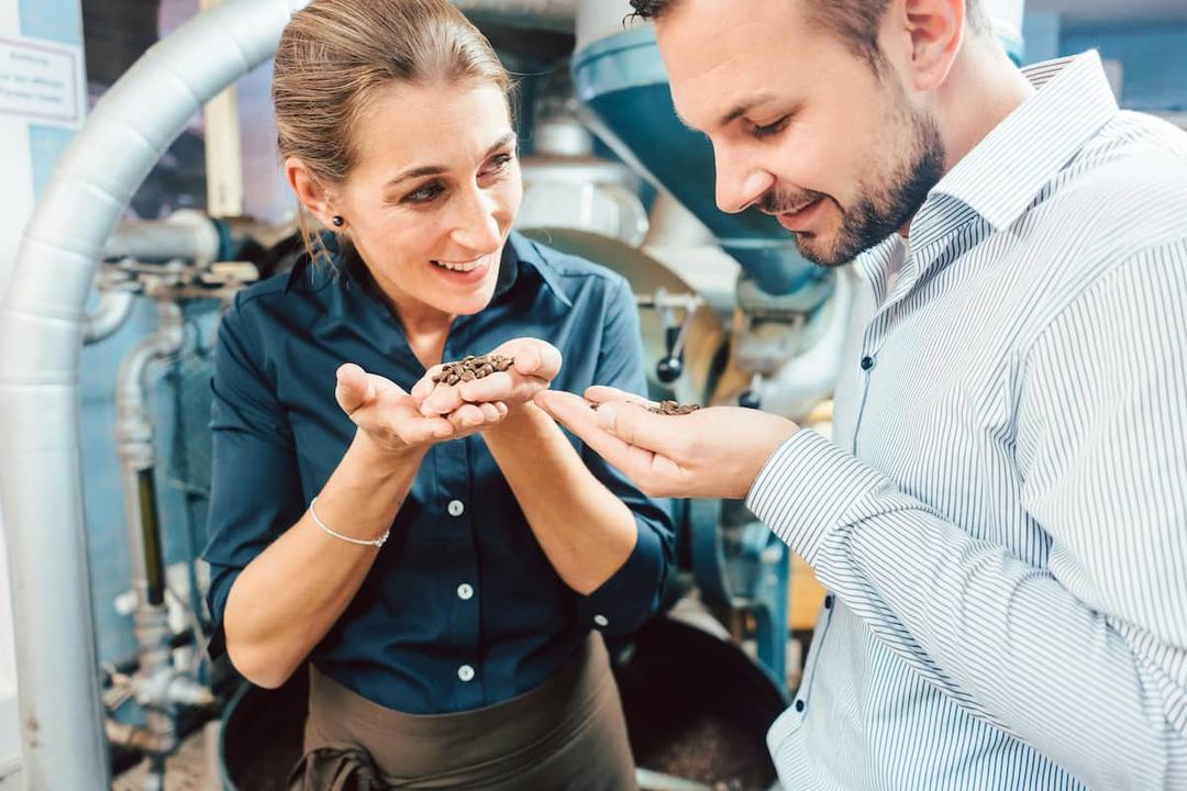 Entrepreneurs smelling coffee beans in a factory setting, illustrating how to test a food product before launching it.