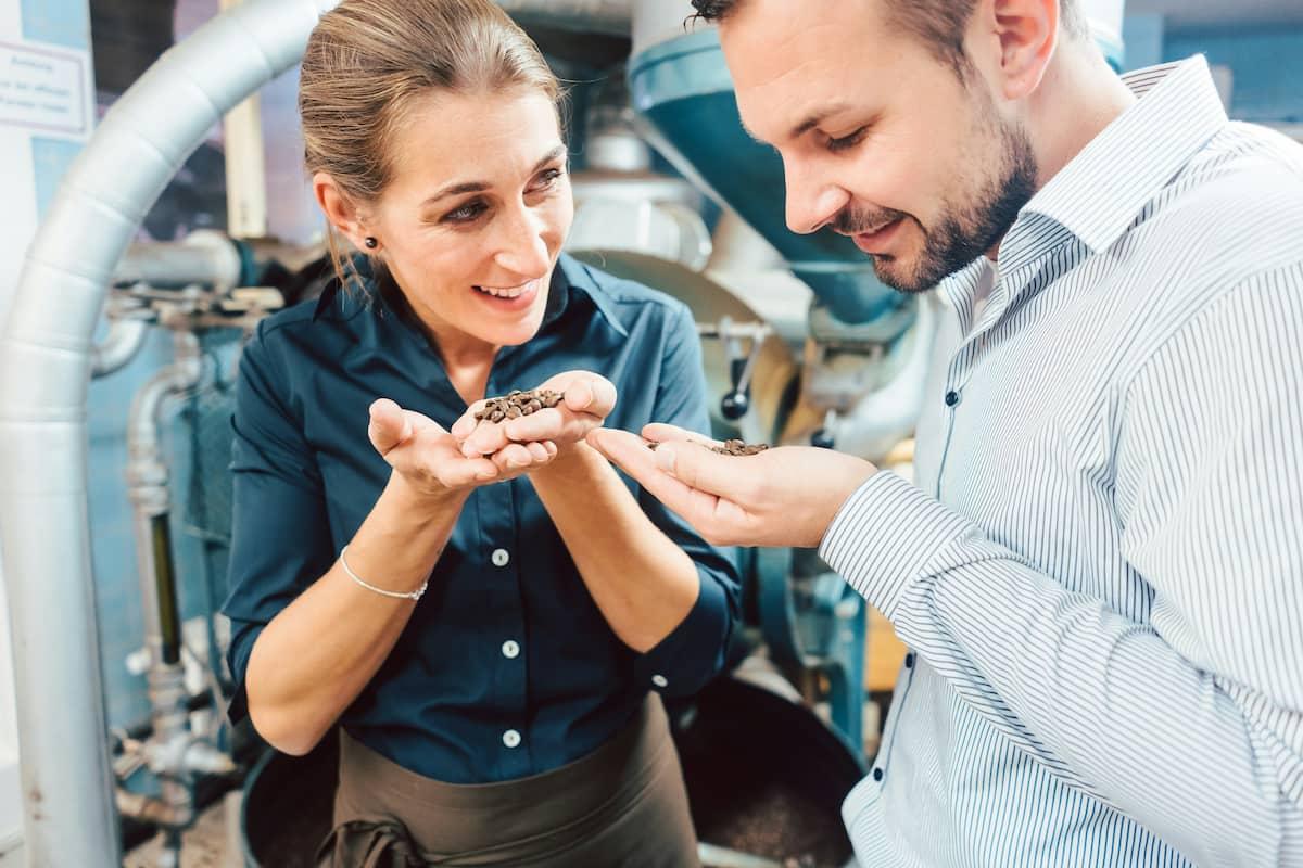 Entrepreneurs smelling coffee beans in a factory setting, illustrating how to test a food product before launching it.