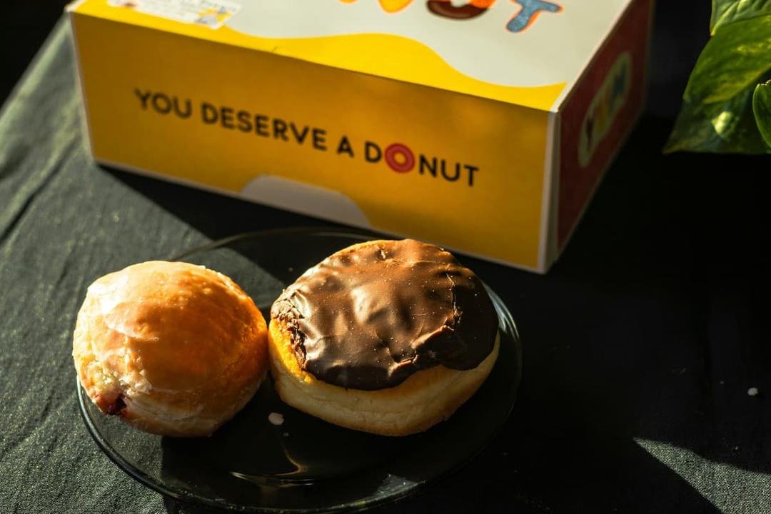 Two donuts on a plate in front of a colorful box, ideal for discussing National Donut Day pricing strategies for delivery restaurants.