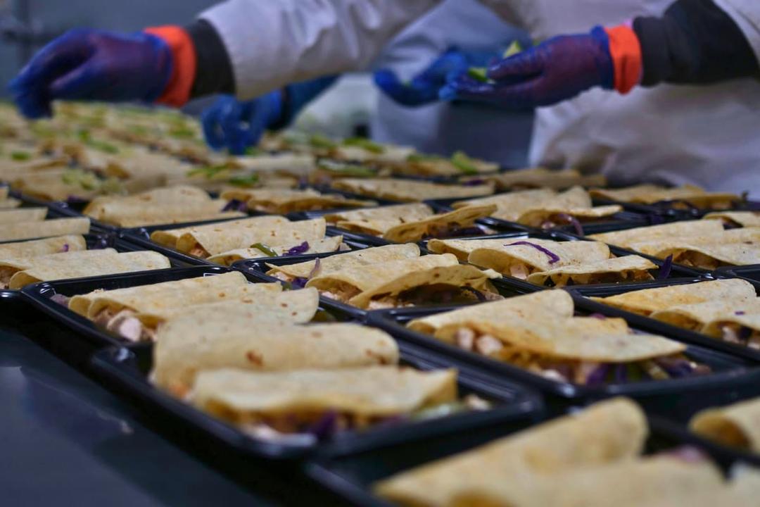 Workers inspect meals in trays as part of quality control tips for small food manufacturing businesses.