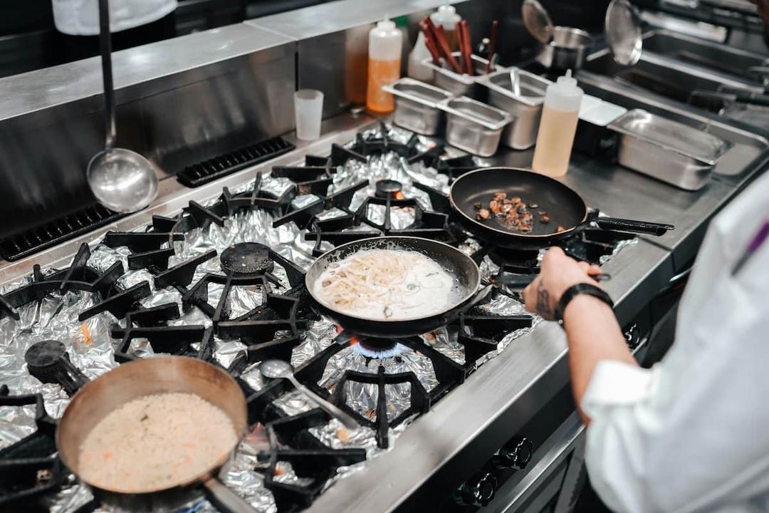 Pots cooking on a stove with foil-lined burners, possibly indicating restaurant health code violations in a commercial kitchen.
